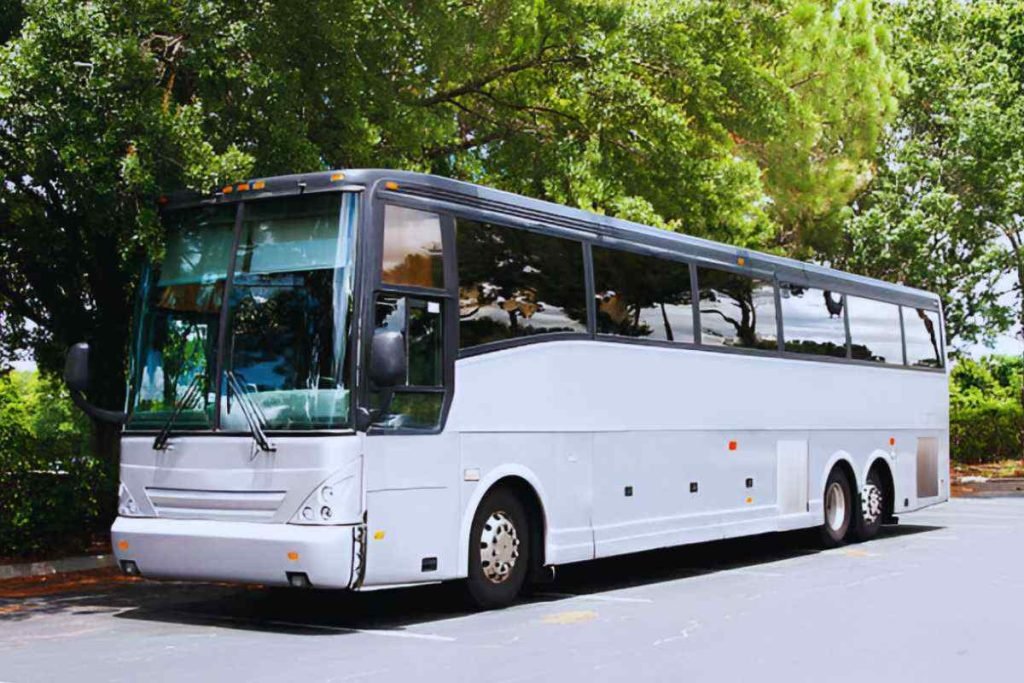 Charter Bus in white color is standing under a tree on a road